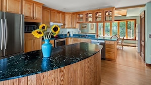 Una cocina moderna con armarios de madera, encimera de mármol negro y una isla grande. Girasoles en un jarrón azul sobre la isla.