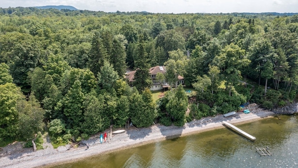 Una propiedad frente al lago con una casa rodeada de bosque denso, un muelle y un bote pequeño.