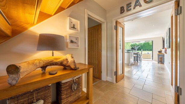 A wooden table with a log centerpiece, a wall-mounted lamp, and framed pictures. A door labeled "BEACH" leads to a kitchen area with a view of the outdoors.