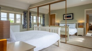 A bedroom with a large bed, a bedside table, a nightstand, a mirror, and a window with curtains.
