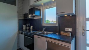 Una cocina moderna con horno empotrado, microondas y cafetera. Hay una ventana sobre el fregadero y una puerta con picaporte a la derecha.