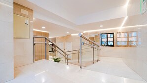 Een nette, moderne lobby met een marmeren vloer, een trap met metalen leuning en een receptiegedeelte met houten afwerking.