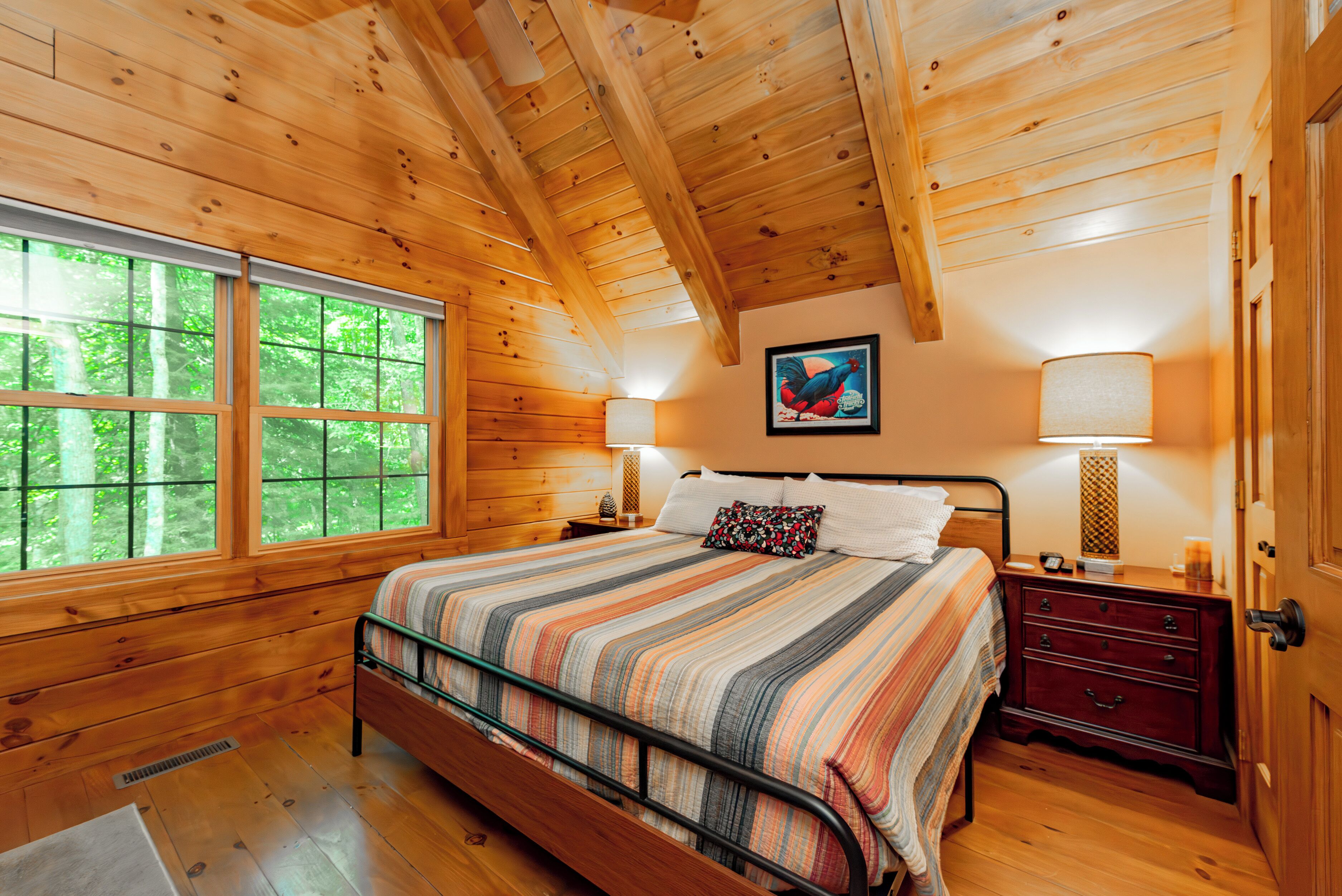 A wooden cabin bedroom with a bed, nightstands, and a window with a view of trees.