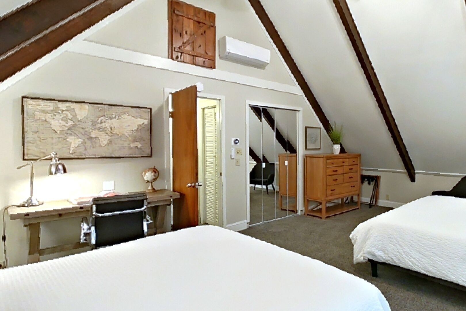 A bedroom with two beds, a desk with a chair, a dresser, and a map on the wall.