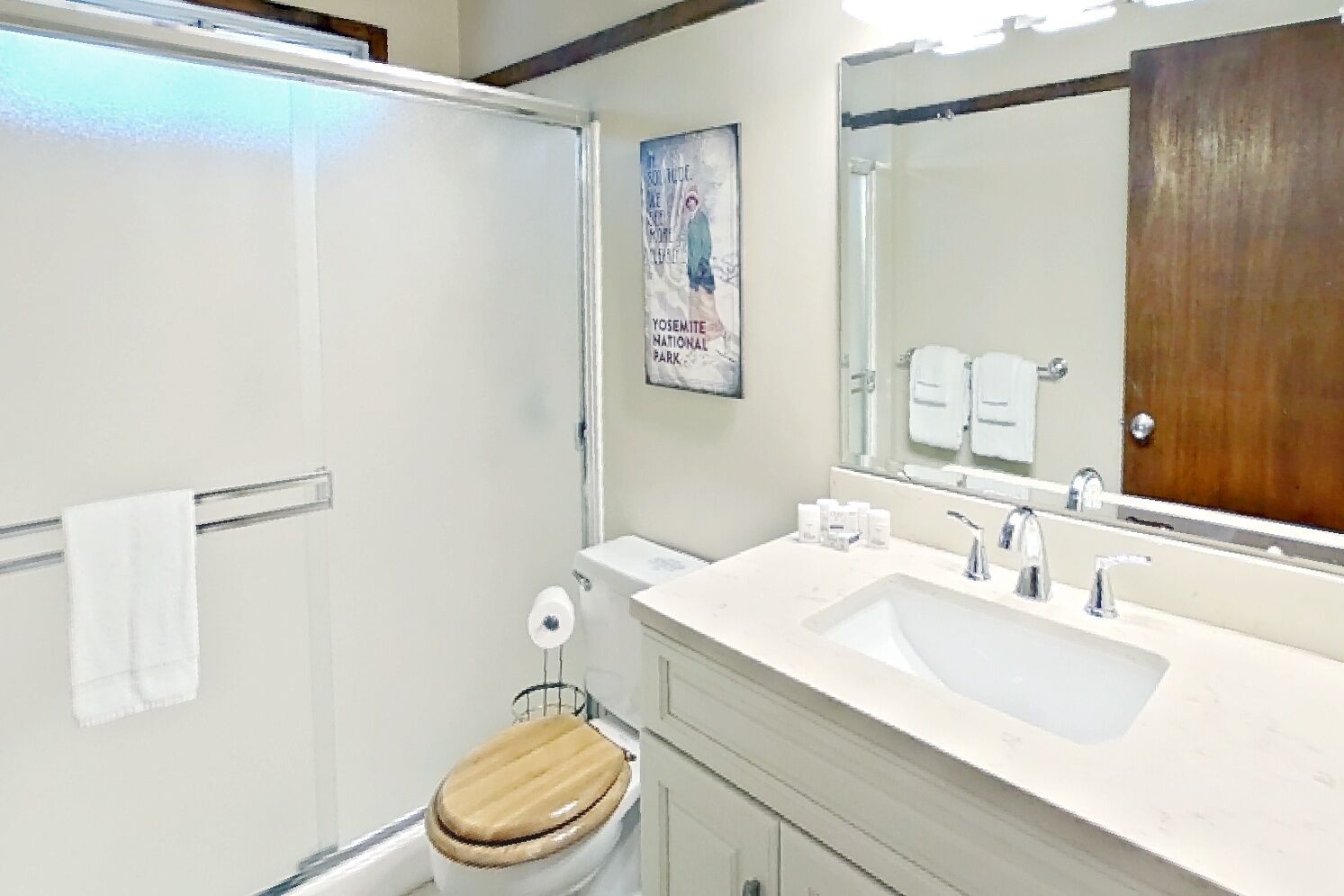 A bathroom with a wooden toilet, a white sink, a large mirror, and a shower.