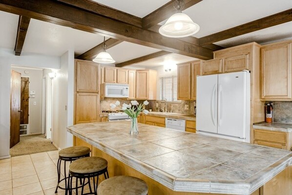 A kitchen with wooden cabinets, a large island with stools, a microwave, a refrigerator, and pendant lighting. - Yosemite Gateway Cabin Valley Views, Sleeps 10 (Groveland)