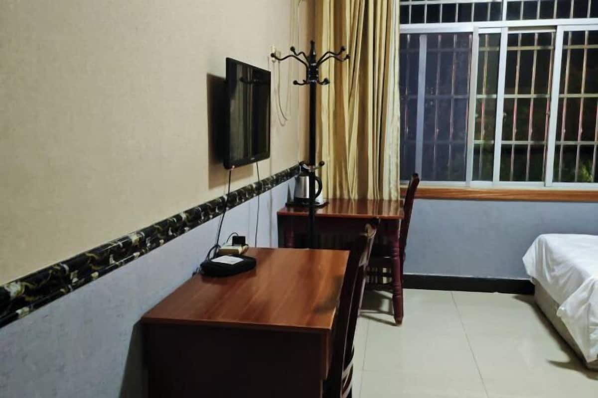Une chambre d’hôtel comprenant un lit, un bureau en bois avec une chaise, un téléviseur fixé au mur et une fenêtre avec des rideaux.