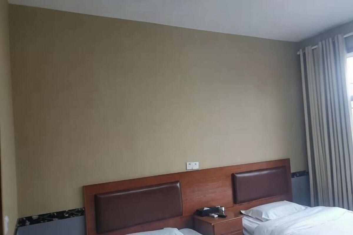 Une chambre d’hôtel avec une tête de lit en bois, une table de chevet et une fenêtre avec des rideaux.