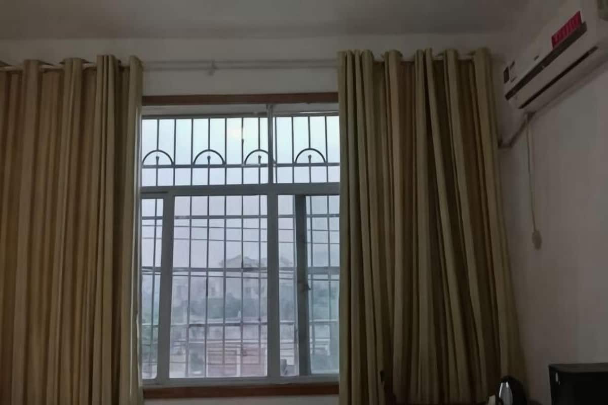 Une pièce dotée d’une grande fenêtre, de rideaux, d’un appareil de climatisation et d’une chaise.
