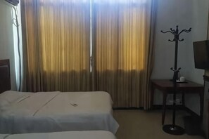 Et hotelværelse med to senge, et knagered, et lille bord og et fjernsyn.