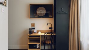 Egy modern szoba, melyben van egy fa íróasztal, egy szék, egy kávéfőző, és egy képkeretbe helyezett tábla, amelyen a következő felirat olvasható: „városi ház”.