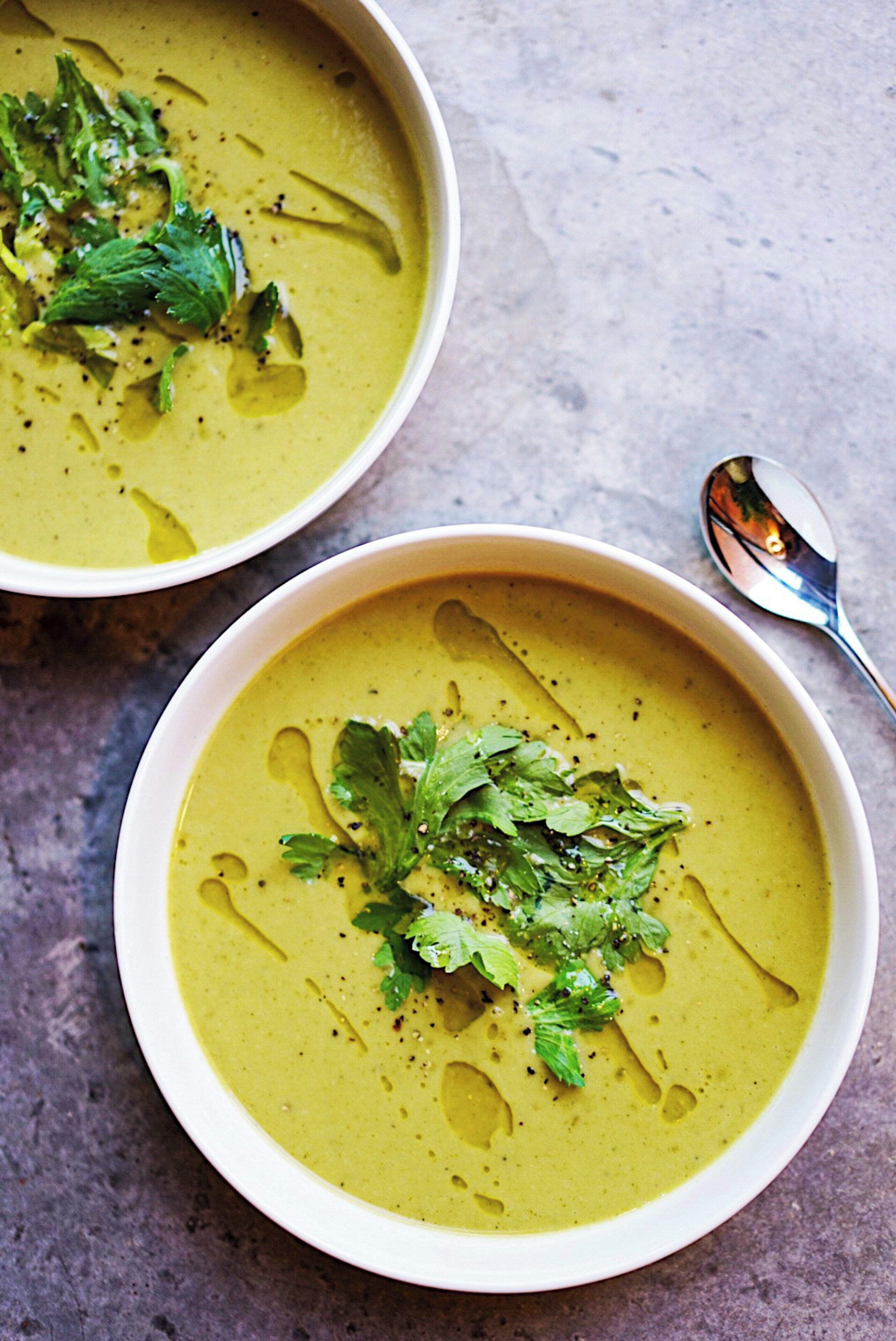 Duas tigelas de sopa verde decoradas com ervas, sobre uma superfície texturizada.