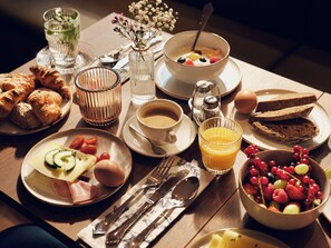 Un desayuno con cruasanes, un tazón de cereal con frutas, un vaso de jugo de naranja y una taza de café.