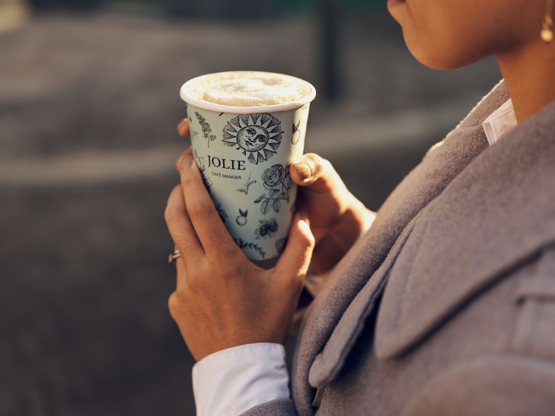A person holding a cup with a floral design and the name 'JOLIE' on it.