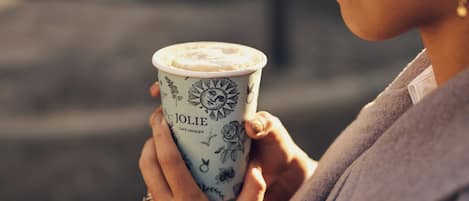 Une personne tenant une tasse ornée de motifs floraux, sur laquelle est inscrit le nom « JOLIE ».