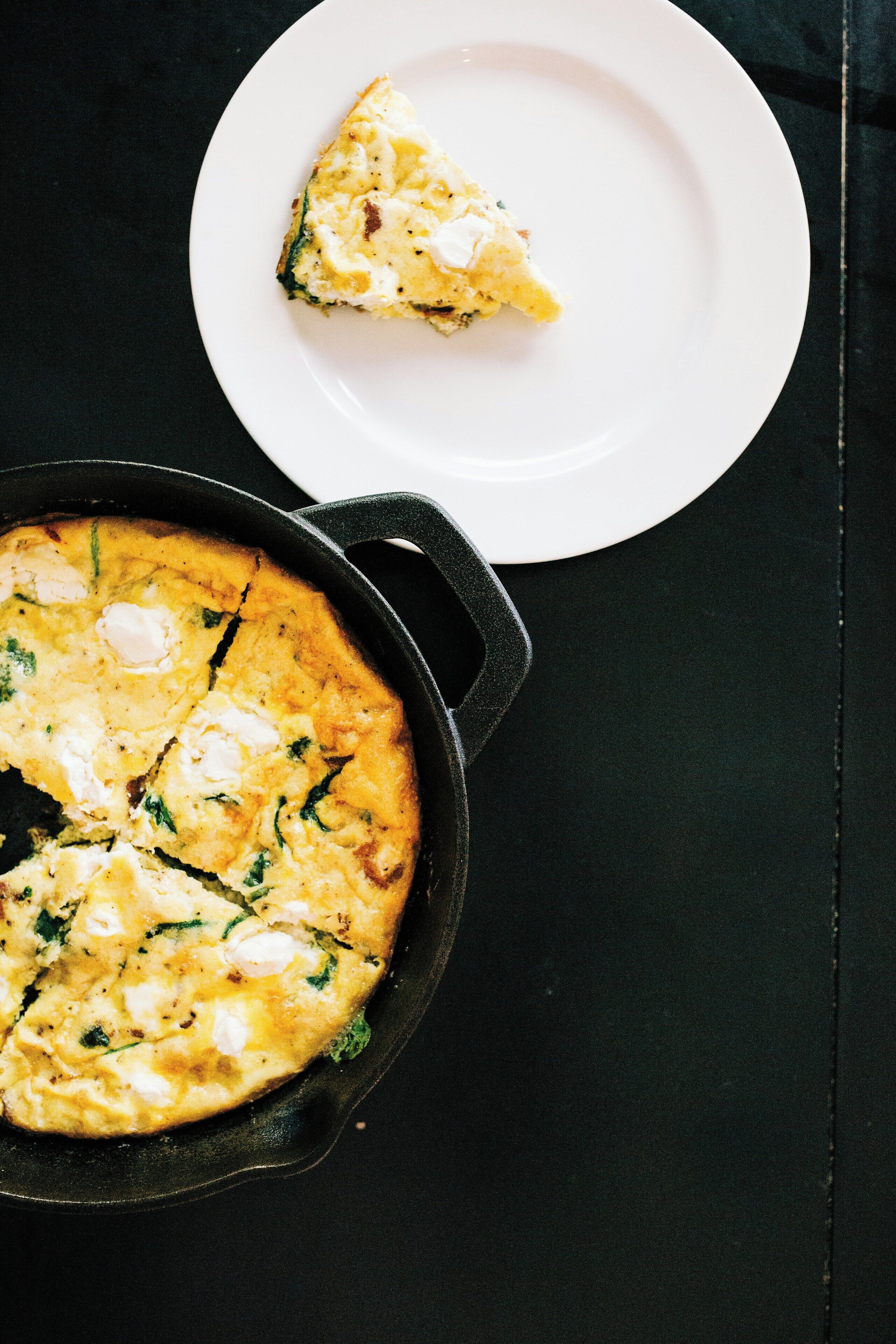 En hvid tallerken med et stykke quiche på et sort bord.