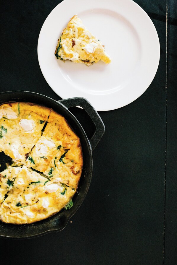 Een witte schaal met een plakje quiche op een zwarte tafel.