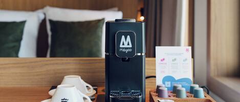 Une machine à café posée sur une table en bois, avec une tasse à café et une barquette de capsules de café.