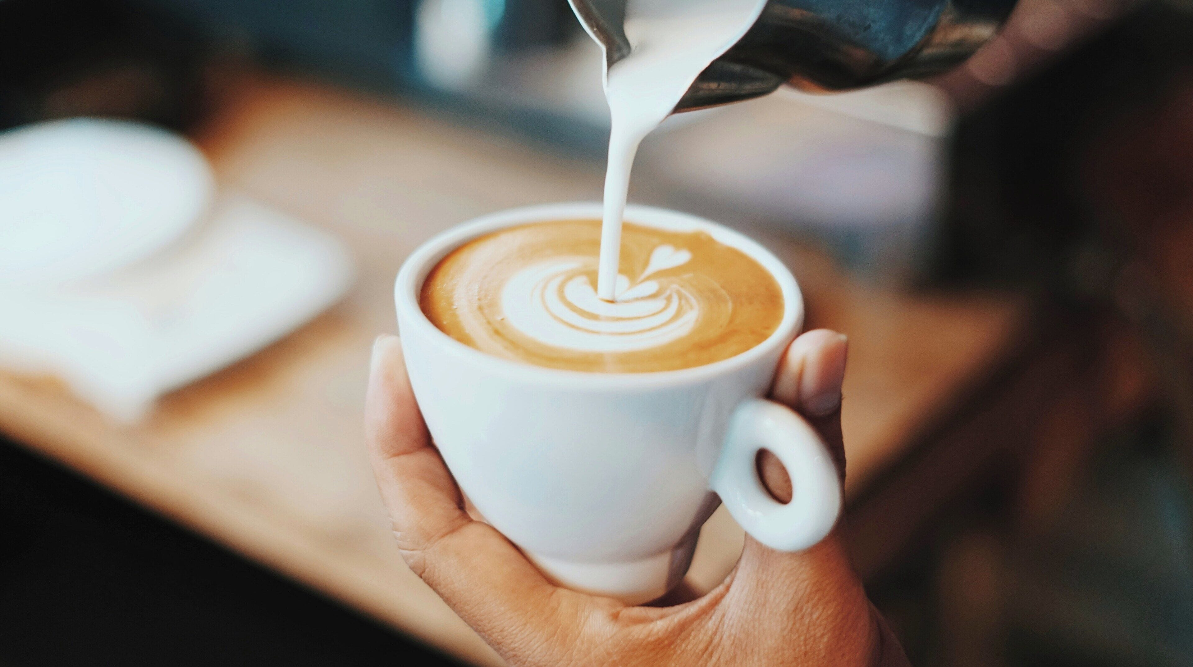Una mano sosteniendo una taza de café con arte latte.