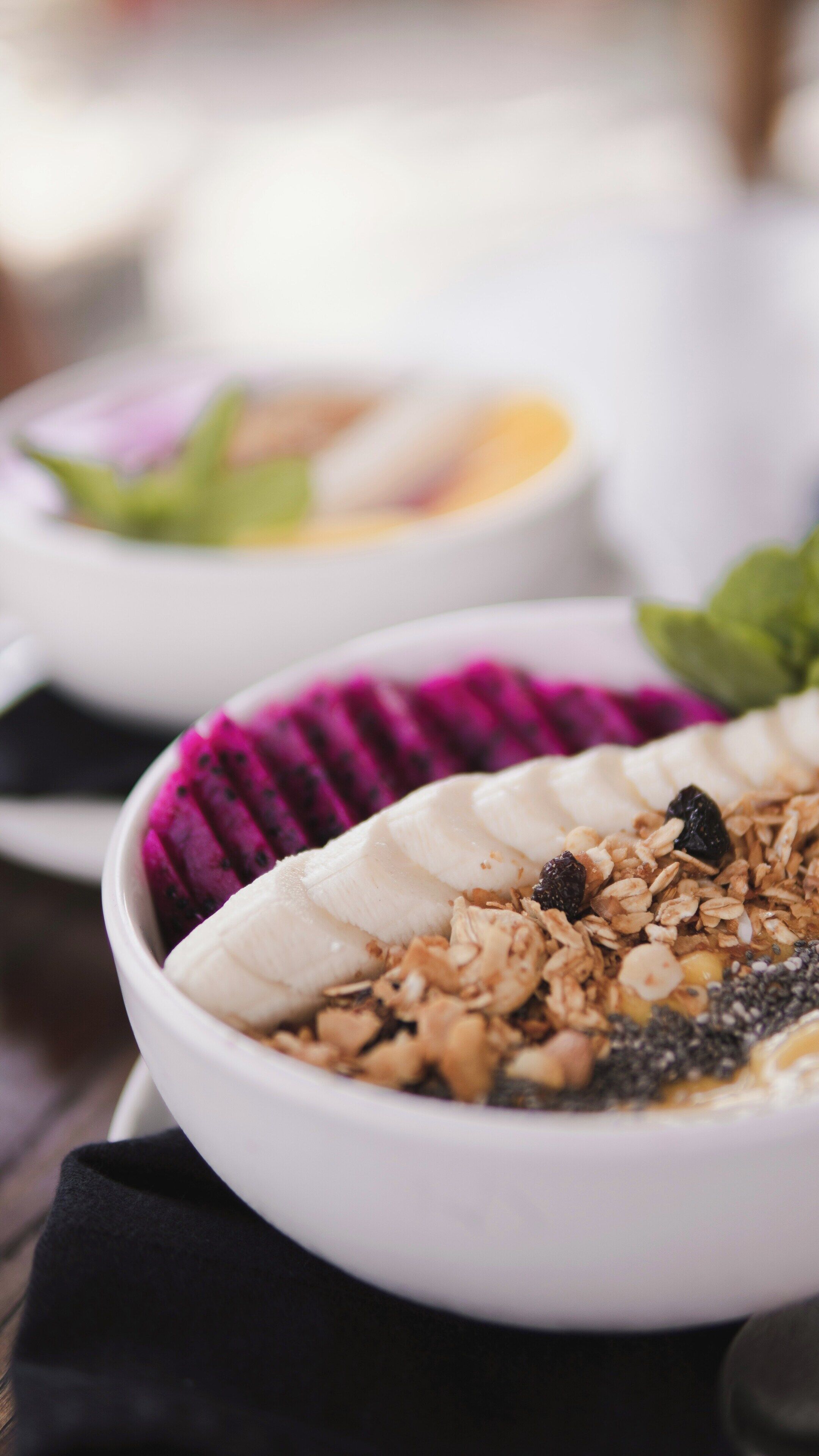 Un plato de comida con una banana, granola y una fruta morada.