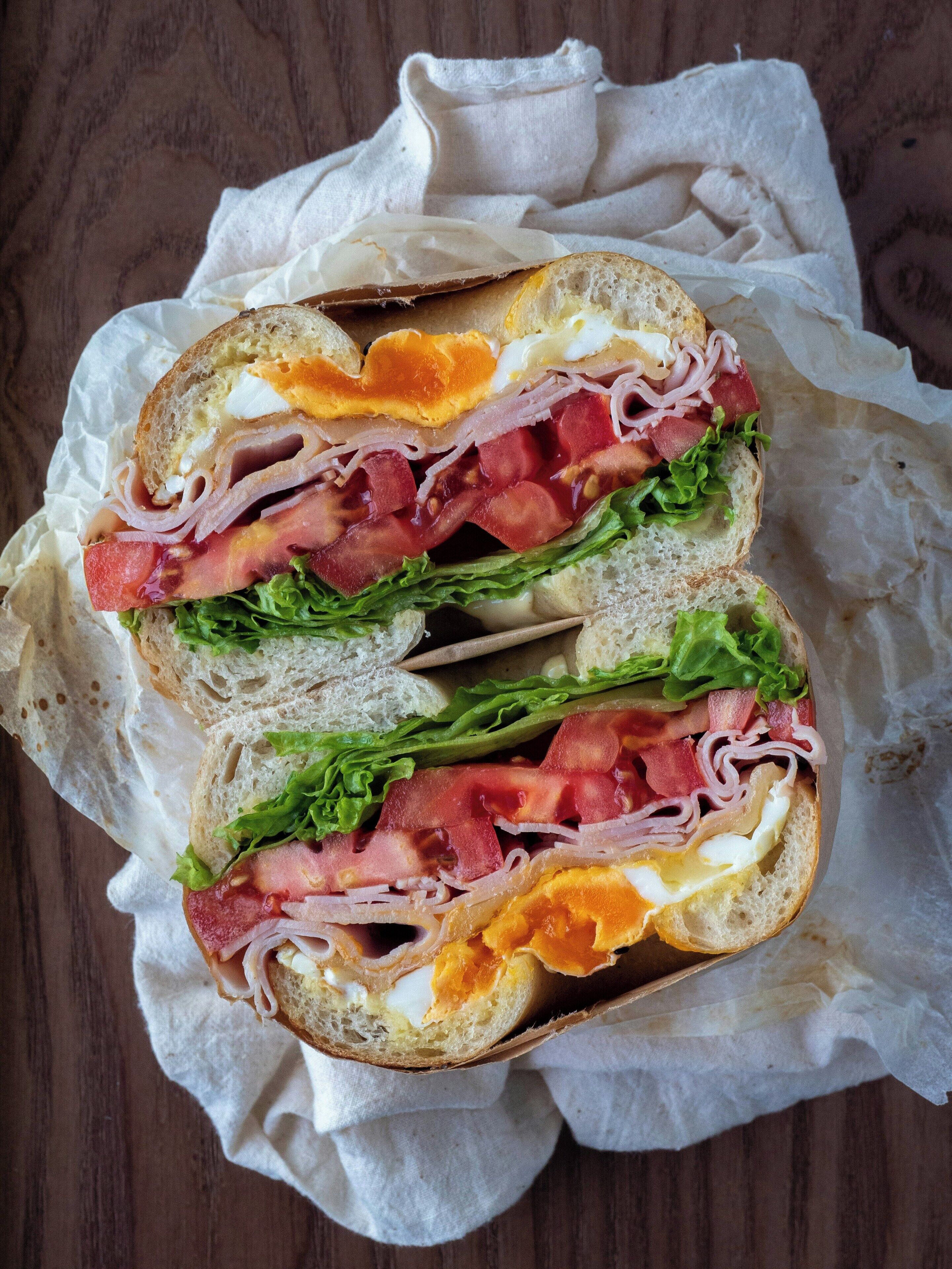 A sandwich cut in half, placed on a piece of paper on a wooden surface.