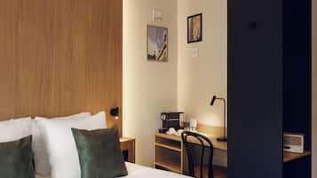 Een hotelkamer met een houten hoofdbord, een bed met witte en groene kussens, een bureau met een lamp en een radio.