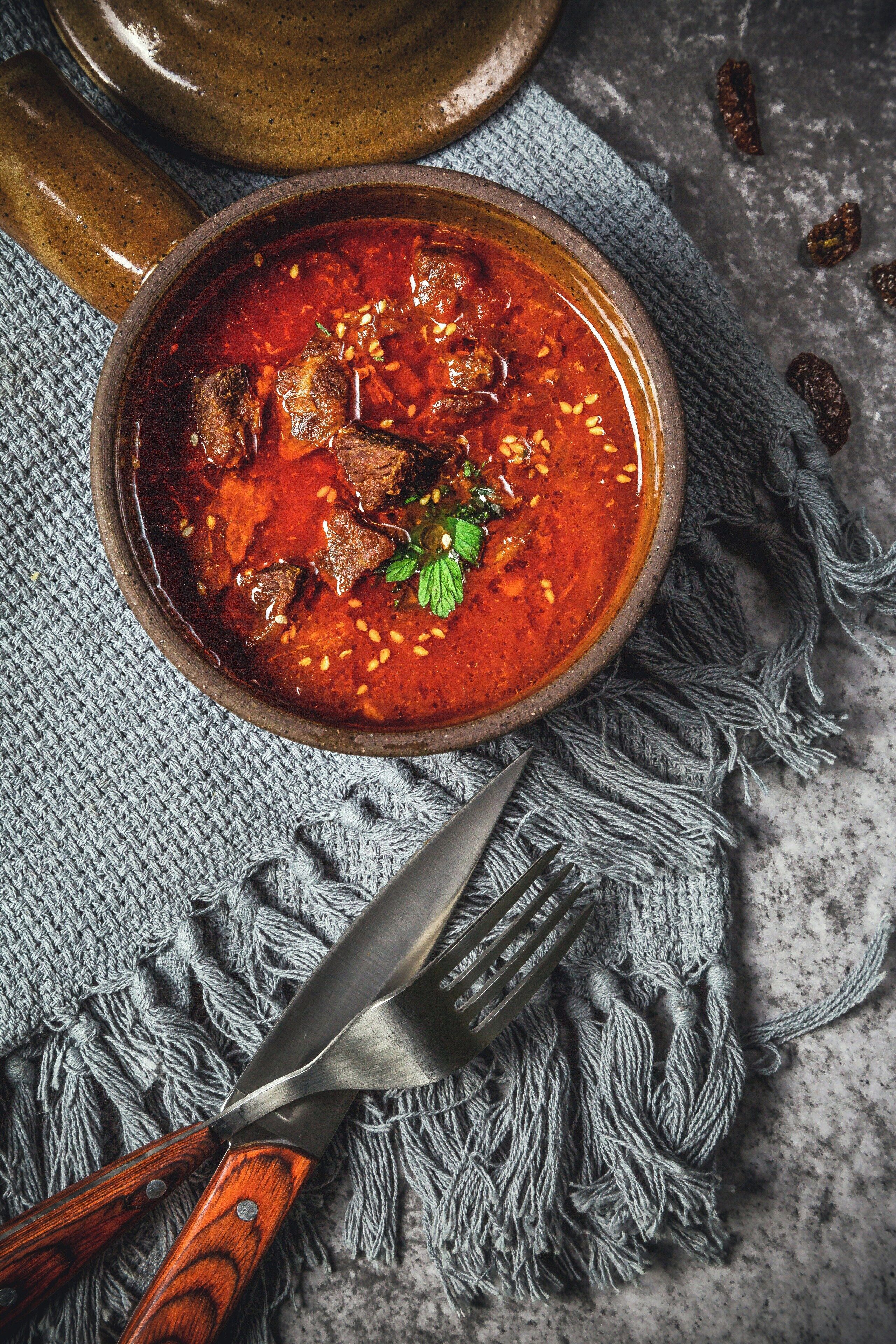 A bowl of stew with a knife and a rustic bowl on a textured cloth.