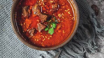 A bowl of stew with a knife and a rustic bowl on a textured cloth.