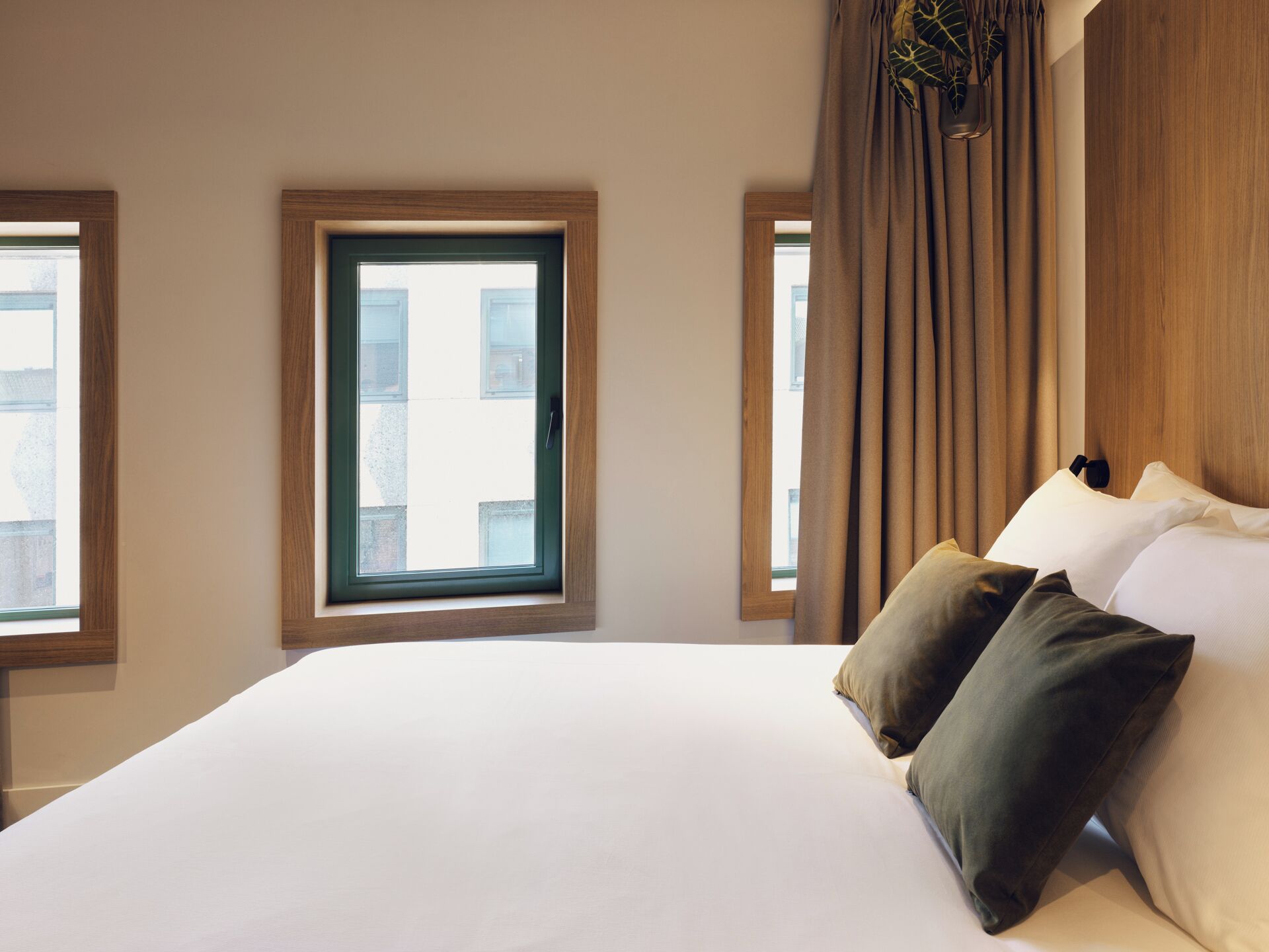 Habitación de hotel con una cama grande, dos ventanas y vistas a edificios.
