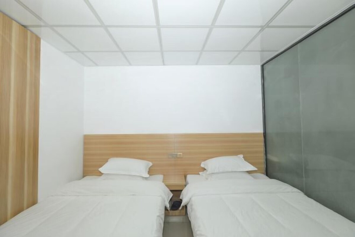Una habitación pequeña y moderna con dos camas individuales, cabecero de madera y separador de vidrio.