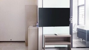 A modern hotel room with a large flat-screen TV mounted on a wall, a small wooden side table, and a grey sofa. - Xinduhui Hotel Shenzhen Dafen Metro Station (Shenzhen)
