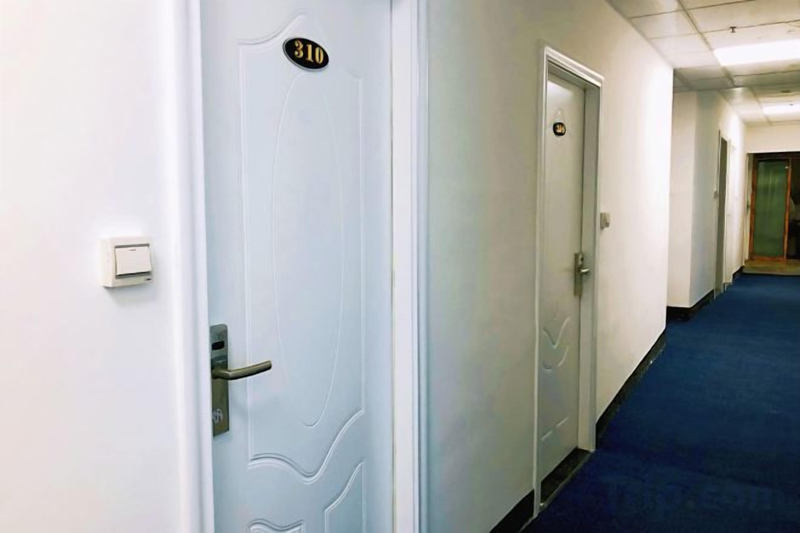 A hotel corridor with a blue carpet, white walls, and doors numbered 310 and 311.