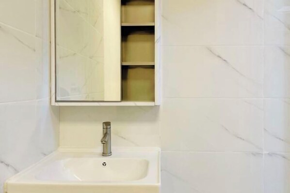 Un baño con un lavamanos blanco, un espejo encima y un estante con cajas de almacenamiento.