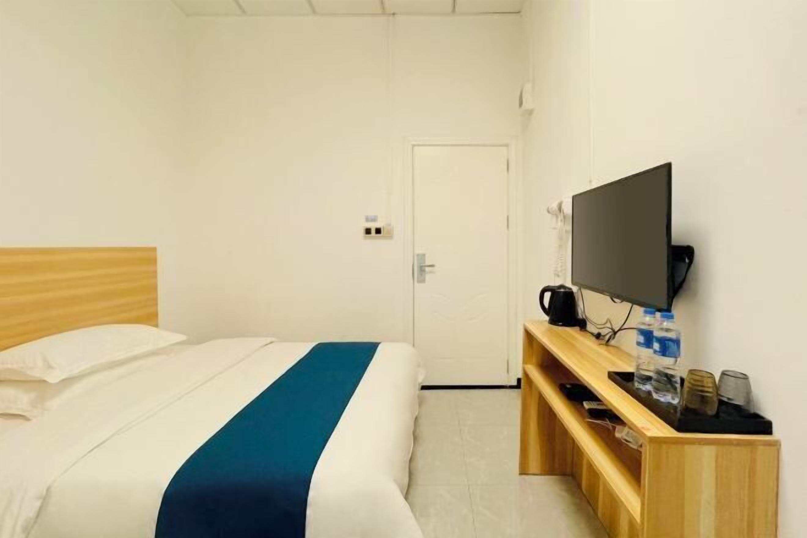 Una habitación de hotel con una cama, un televisor, una mesita de madera y una puerta al fondo.