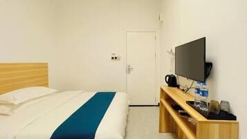 Una habitación de hotel con una cama, un televisor, una mesita de madera y una puerta al fondo.