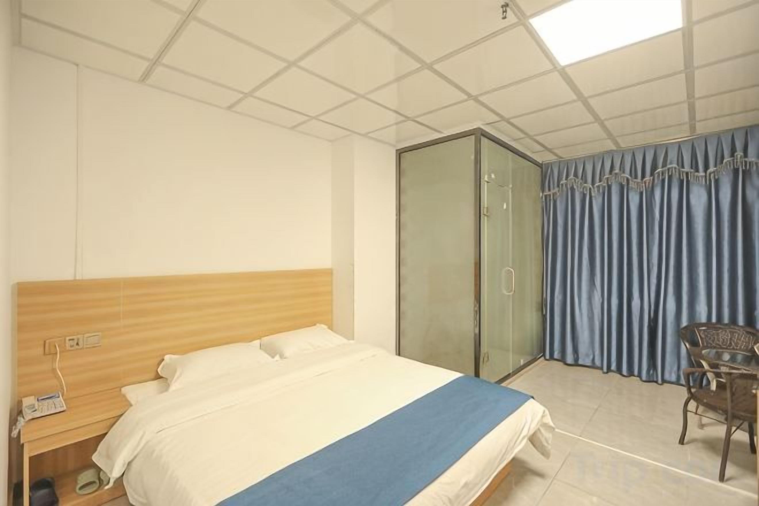 A hotel room with a bed, a wardrobe, a chair, and a desk with a telephone.