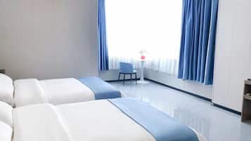 A hotel room with two beds, a small table with a chair, and a window with curtains.