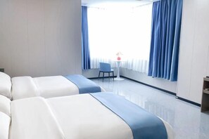 Habitación de hotel con dos camas, una mesita con una silla y una ventana con cortinas.