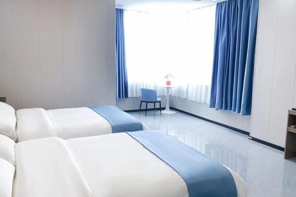 A hotel room with two beds, a small table with a chair, and a window with curtains.