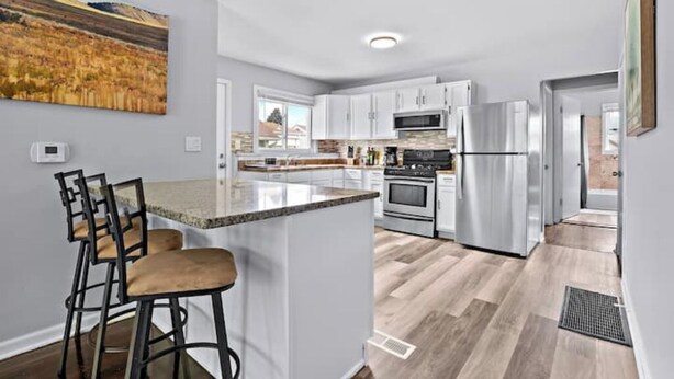 A modern kitchen with white cabinets, stainless steel appliances, and a bar area with stools.