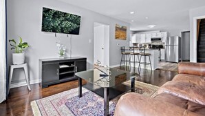A modern living room with a glass coffee table, leather sofa, and a kitchen in the background.