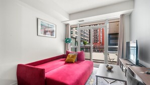 A modern hotel room with a red sofa, a small table, a TV, and a balcony with a city view.