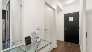 A hallway with a glass display table, white walls, a black door, and a refrigerator in the background.