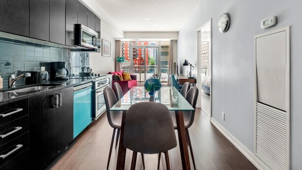 A modern kitchen with dark cabinetry, a glass-top dining table, and a view of a cityscape through large windows.