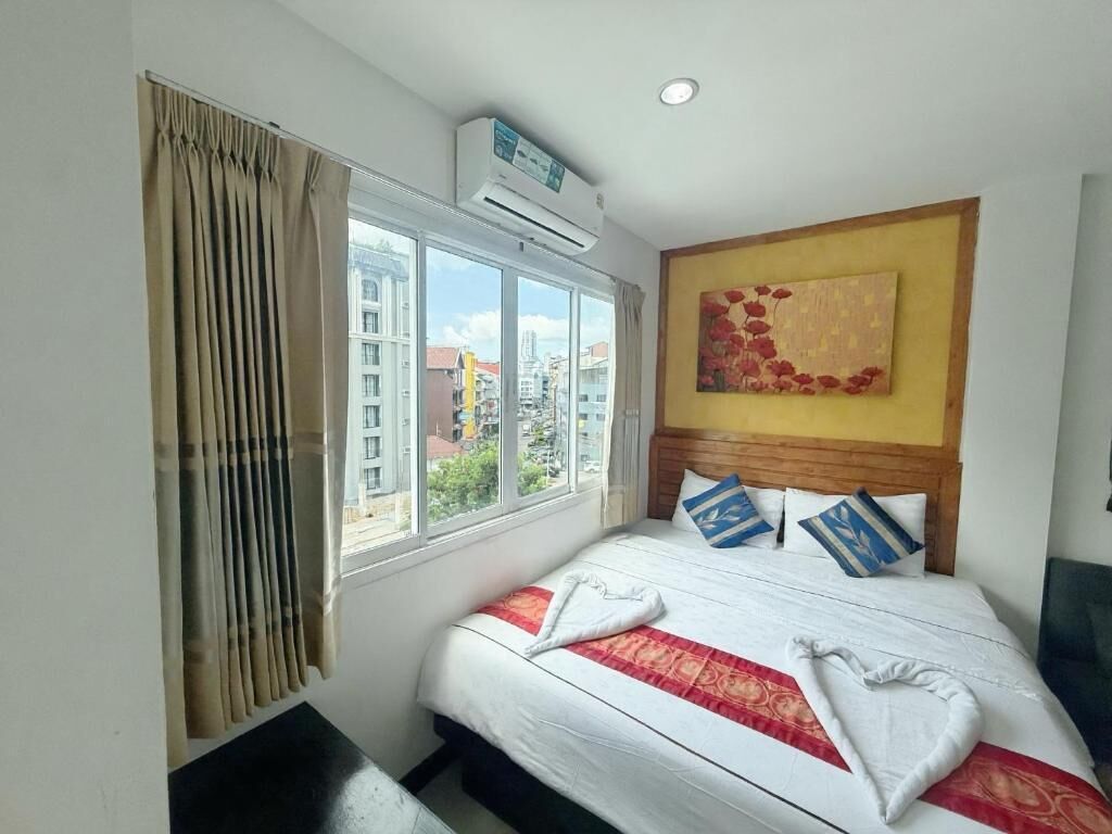 A hotel room with a large bed, a window with curtains, an air conditioning unit, and a city view.