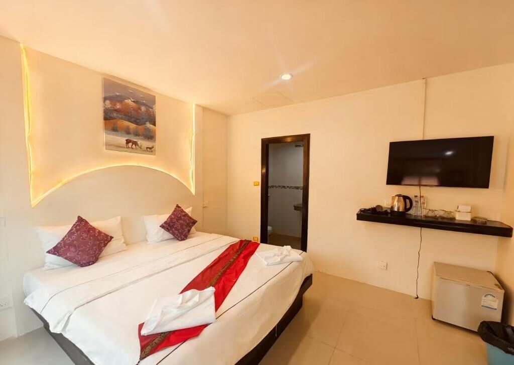 A hotel room with a bed, a TV mounted on the wall, a small kitchenette, and a painting on the wall.