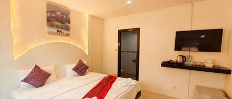 A hotel room with a bed, a TV mounted on the wall, a small kitchenette, and a painting on the wall.