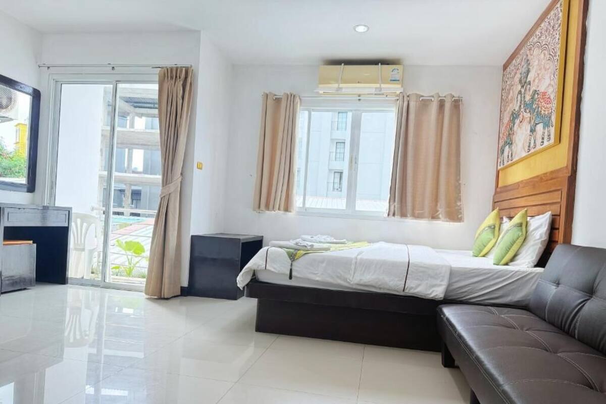 A modern hotel room with a bed, a sofa, a desk, and a large window with curtains.