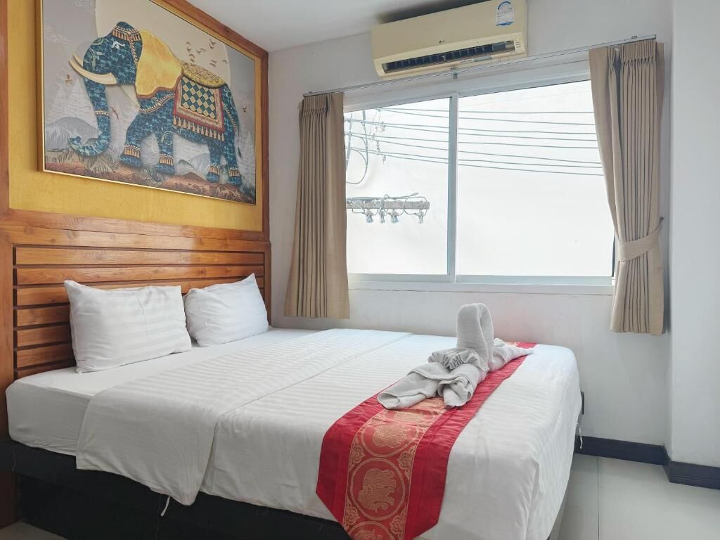 Habitación de hotel con una cama grande, cabecera de madera, ventana con cortinas y un equipo de aire acondicionado.