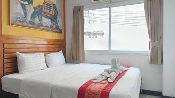 Habitación de hotel con una cama grande, cabecera de madera, ventana con cortinas y un equipo de aire acondicionado.
